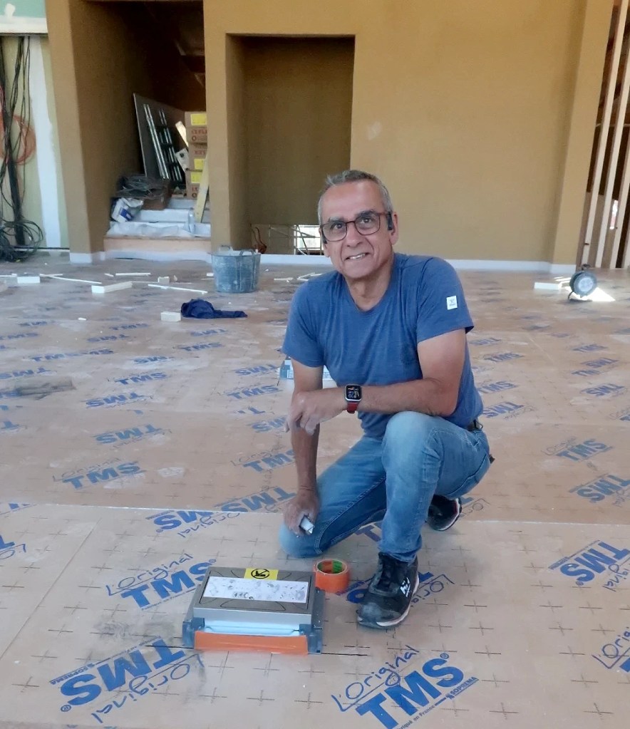 Sur le chantier de la médiathèque de Quincié, Sylvain Antoine au travail un genou au sol, face à l'objectif.